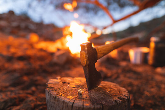 Close-up of axe on tree stump in front of burning campfire at forest during dusk