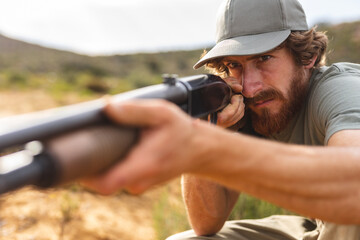 Confident young bearded caucasian man aiming rifle while hunting in forest