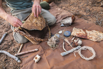 Midsection of young male caucasian survivalist with handmade leather bag kneeling by various objects