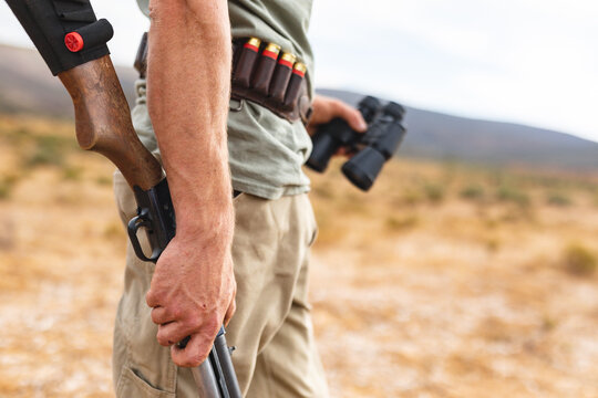 Midsection of young man hunter holding rifle and binoculars in forest - Powered by Adobe
