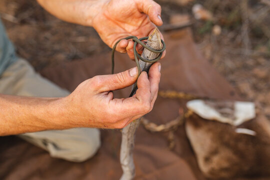 Cropped hands of young male caucasian survivalist tying string on stick while making hunting trap