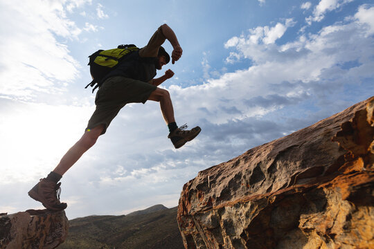 Low angle view of athletic young male caucasian hiker jumping on rocky cliffs during sunny day