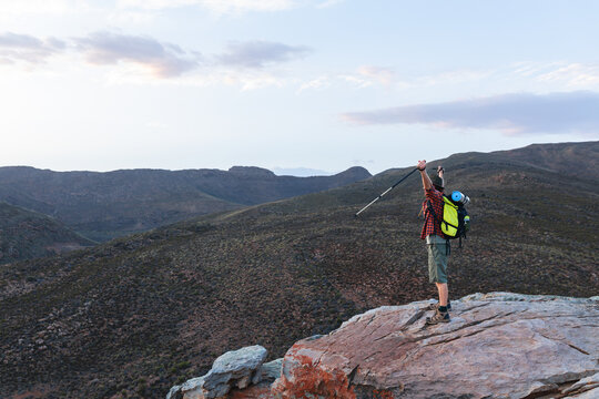 Full length side view of young male caucasian hiker cheering successful from mountain top