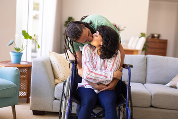 African american man hugging and kissing his disabled wife on wheelchair at home