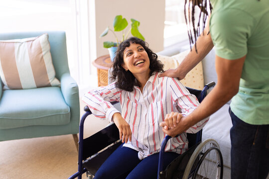 Mid section of a man holding hands of his disabled wife sitting on wheelchair at home