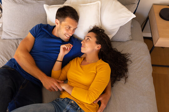 Caucasian couple holding hands looking at each other while lying on the bed