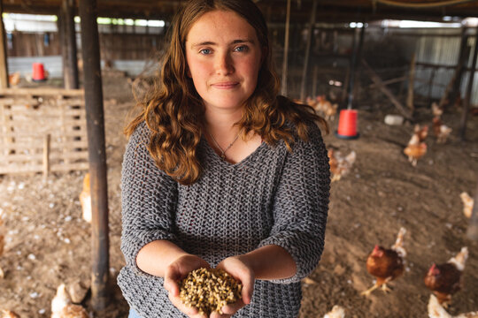 Portrait of beautiful young female homesteader with grain pellets in cupped hands in chicken pen