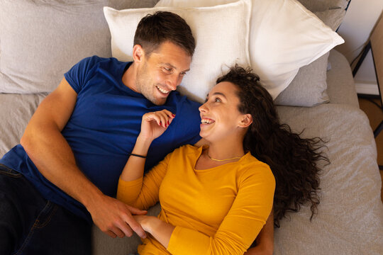 Caucasian couple holding hands looking at each other while lying on the bed