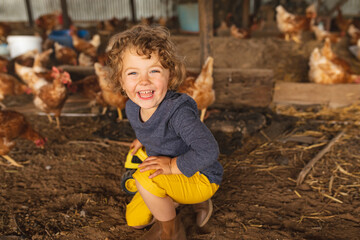 Portrait of happy cute boy kneeling with hens in background at poultry farm