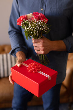 Mid section of a man holding a flower bouquet and gift box