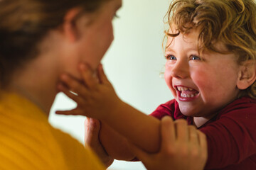 Smiling blond boy playing while touching mother's cheek in kitchen at home