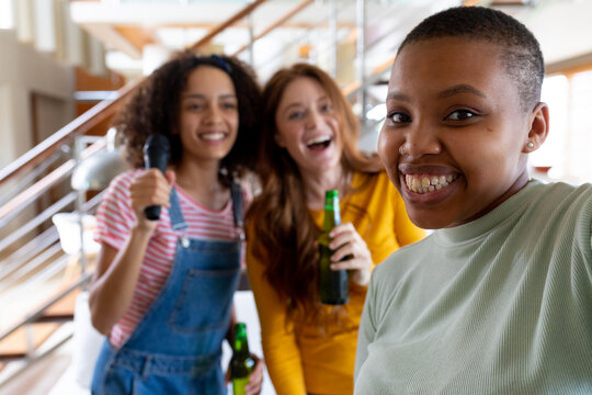 Happy woman taking selfie with multiracial female friends holding beer bottles at home
