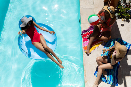 Multiracial female friends in hats enjoying weekend at swimming pool on sunny day