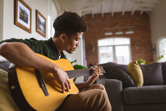 Young biracial man practicing acoustic guitar in living room at home