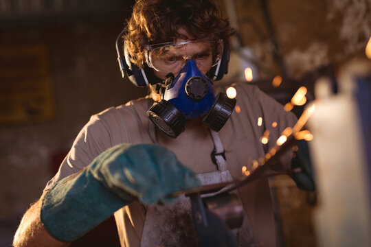 Caucasian blacksmith wearing gas mask while working on metal in industry
