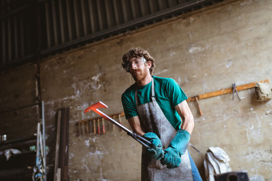 Caucasian blacksmith in protective eyewear and gloves forging in metal industry