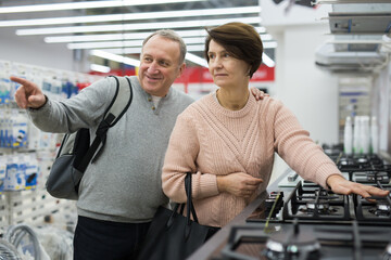 Fototapeta na wymiar Middle aged wife and husband picking new gas stove in shop of household appliances. Man pointing finger.