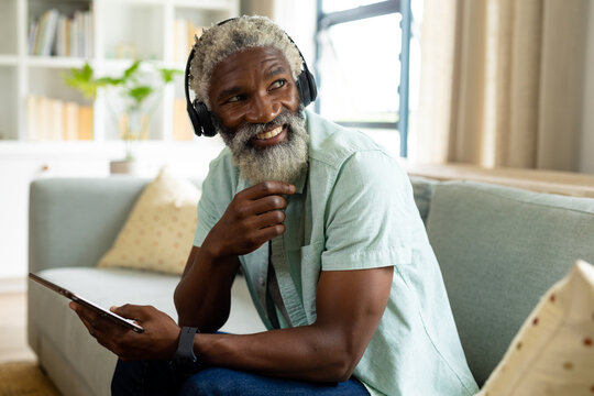 Smiling African American Man Listening Music Through Headphones While Sitting With Digital Tablet