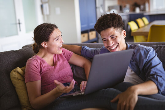 Cheerful young biracial couple enjoying while discussing over laptop in living room at home