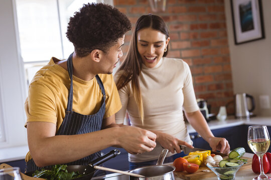 Happy young biracial couple cooking meal together in kitchen at home