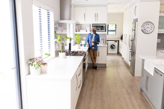 African american man looking away holding digital tablet standing in kitchen at home