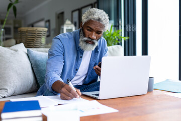 Confident african american senior male freelancer working with laptop and smartphone