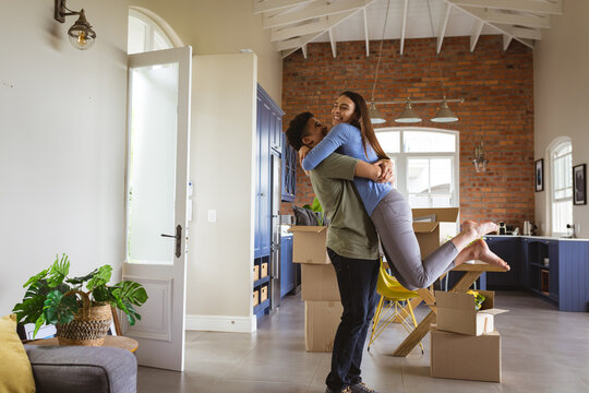 Excited young man lifting girlfriend by cardboard boxes in new home