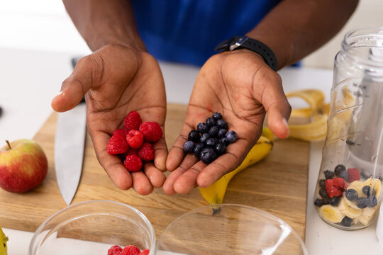 Hands of african american man holding fresh raspberries and blueberries in kitchen at home