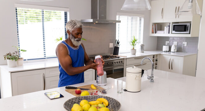 Senior african american man preparing healthy fruit smoothie in kitchen at home