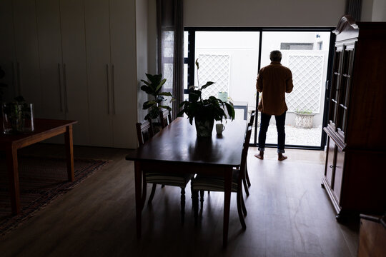 Full length rear view of senior african american man standing by window in living room at home