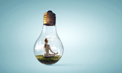 Business woman doing yoga in lotus pose inside light bulb