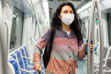 Obraz premium Positive woman passenger in face mask for disease protection standing in subway car, using public transport in big city
