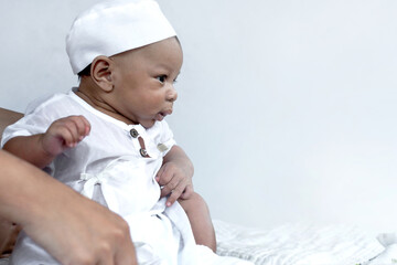 Cute 2 months old Muslim baby boy wearing white hat and Muslim Men's robe costume, isolated on white background, looking at something