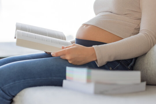Prenatal book reading pregnant woman holding books sitting on sofa at home. Pregnancy lifestyle preparing for birth and raising a child