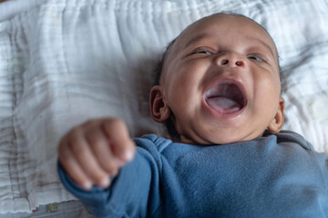 Happy two months old African baby boy laughing on white mattress, view from above