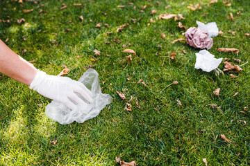hand grabbing plastic bags and wrappers from green lawn in a park, cleaning up and respecting the...