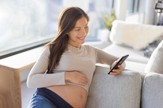 Pregnant Asian woman happy using mobile phone app for shopping or telemedicine. Pregnancy lifestyle at home
