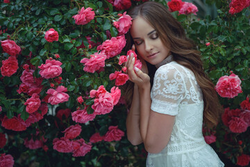 Beautiful portrait of a woman in poses. A brunette woman is standing next to roses in nature.