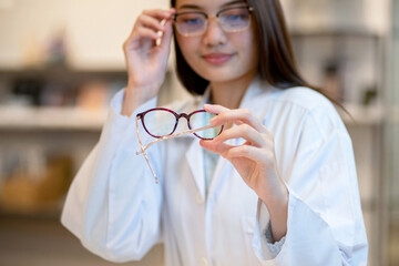 Female optometrist or optician wearing lap coat checking eyeglasses details in a shop, selective focus