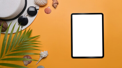 Digital tablet, traveler accessories, seashells and tropical palm leaves on yellow background. Travel, summer and holiday concept.