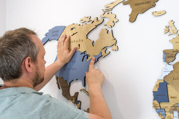 A man points his finger at the Ottawa, Canada on a wooden map of the world.