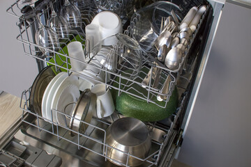 Open door of the built-in dishwasher with clean dishes inside.