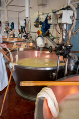 Fototapeta na wymiar Process of making wheels of parmigiano-reggiano parmesan cheese on small cheese farm in Parma, Italy, copper-lined vats with curd