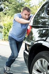 a man pushing broken car on road along city street