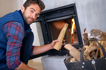 This should warm things up. Shot of a young man building a fire in his fireplace at home.