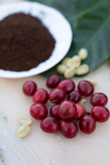 Red ripe arabica coffee berries, green coffee beands, leaves and roasted ground coffee in bowl