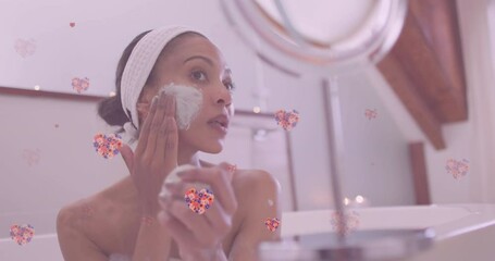 Animation of floral hearts over smiling african american mother and daughter pampering in bathroom