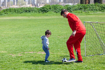 Father with his little son playing football, soccer in the park. Father teaches his son