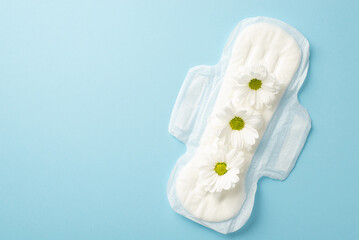 Top view photo of sanitary napkin with camomile buds on isolated pastel blue background with copyspace - obrazy, fototapety, plakaty