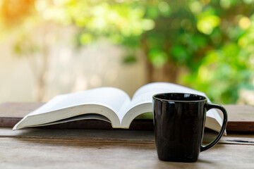 The open book and black coffee cup on the wooden infront of house.